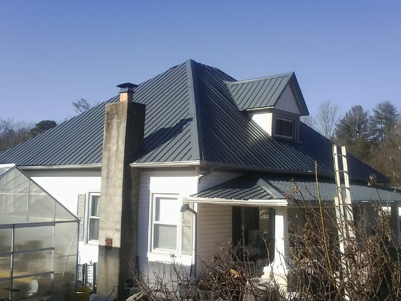 Dark blue standing seam metal roof on a white farmhouse with dormer — Slate & Tile Roof Repair by Roofing Brothers in Monument Beach
