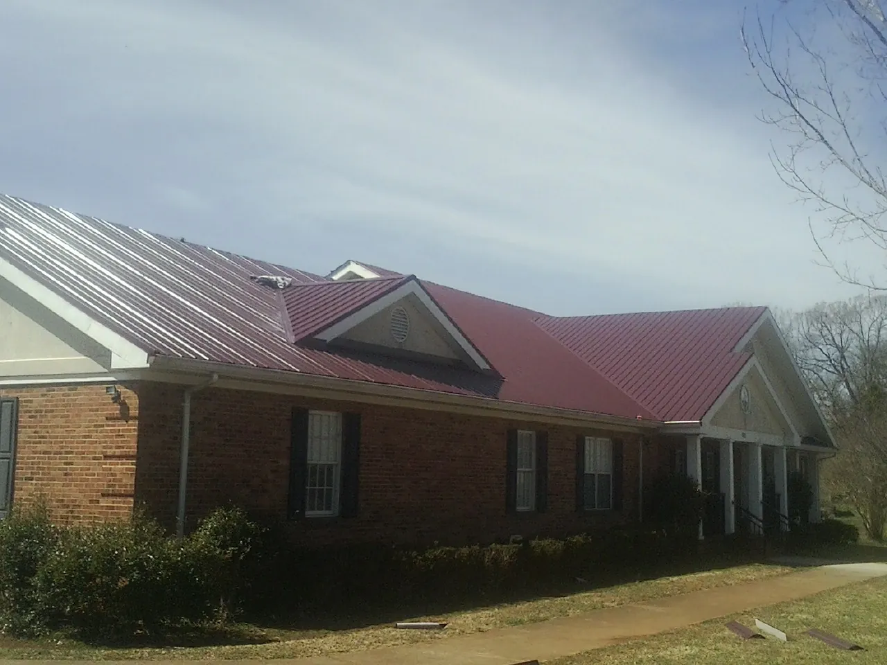Red metal roof with gabled entries on a long brick building, from a Hail Damage Roof Repair job in Monument Beach