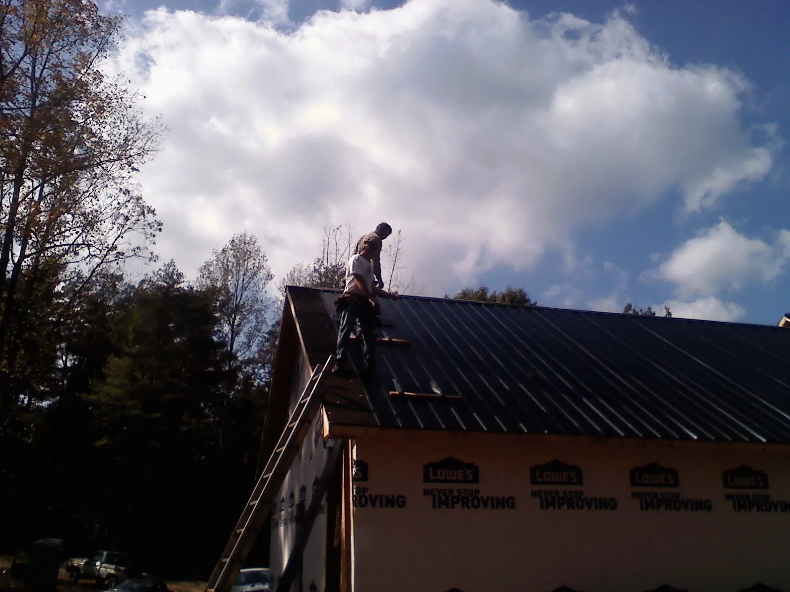 Roofer fastening dark metal panels high against a cloudy sky, from a Roof Inspection job in Monument Beach
