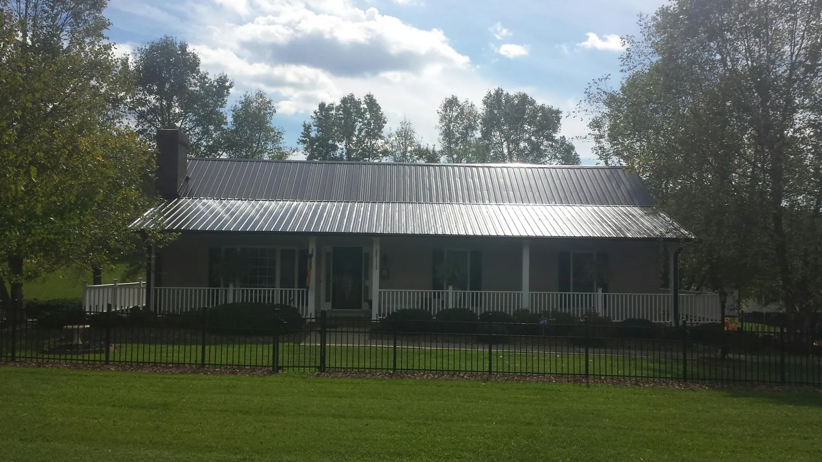 Gray metal roof on a brick ranch with a full width front porch — Gutter Guard Installation work by our crew in Monument Beach