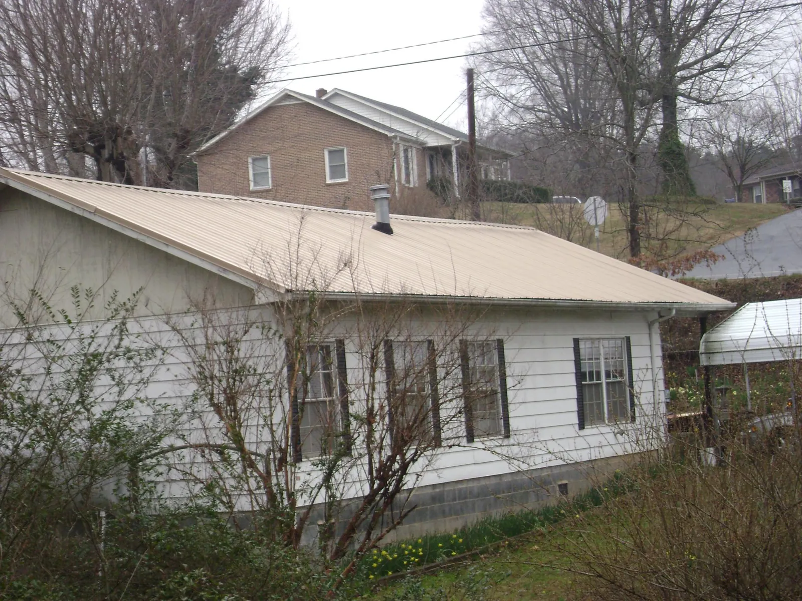 Tan metal roof on a white sided house set into a hillside — Commercial Roofing by Roofing Brothers in Monument Beach