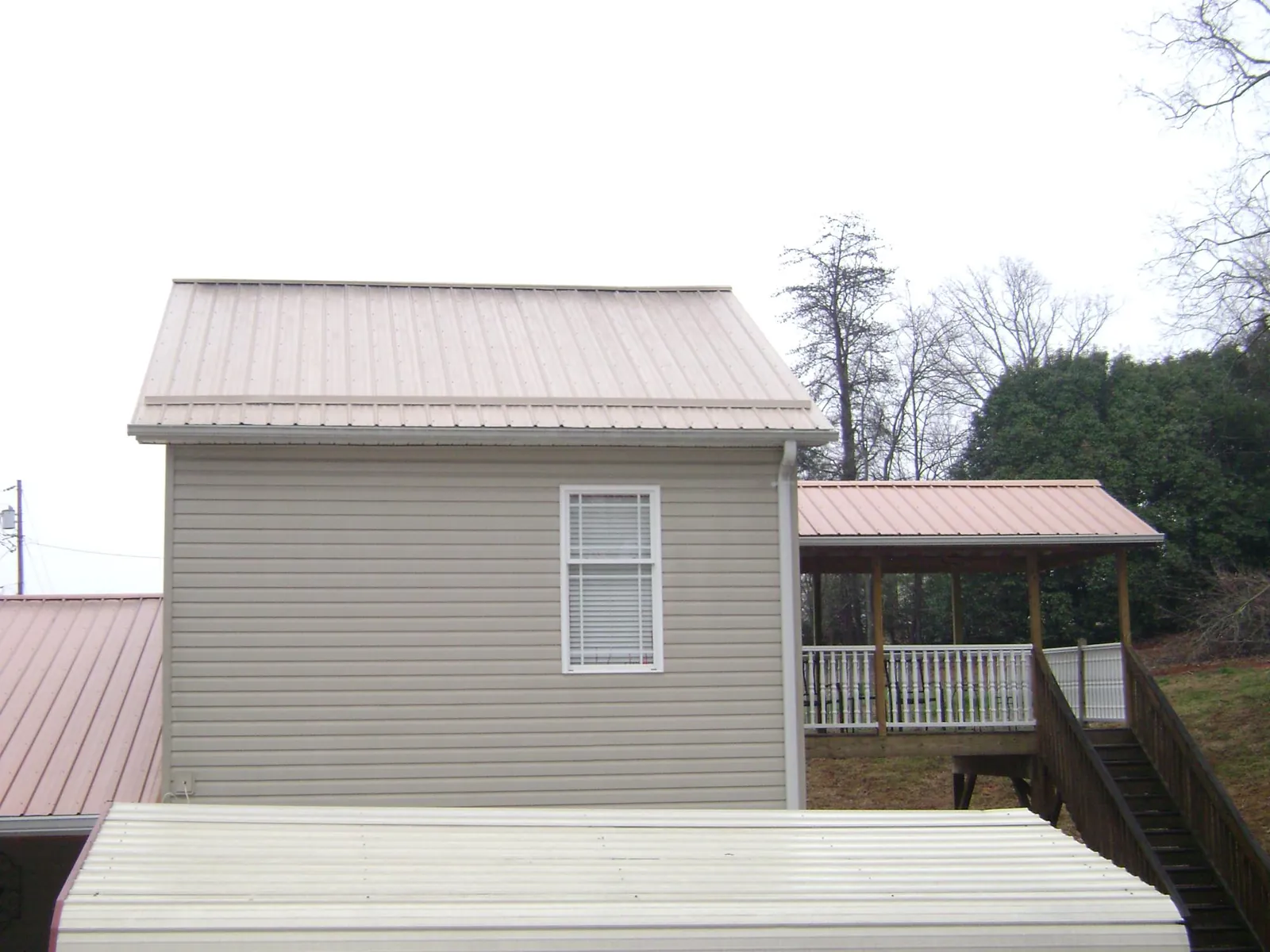 Tan metal roofs on a two story addition and attached porch, from a Roof Replacement job in Monument Beach